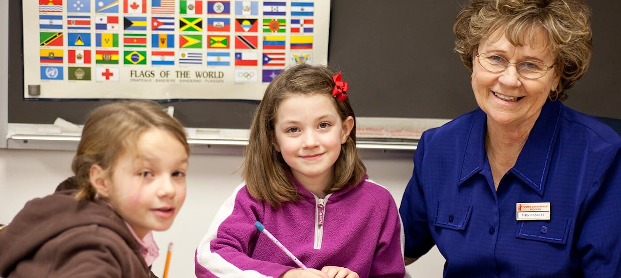 A Foster a Grandparent program volunteer smiles with two children..