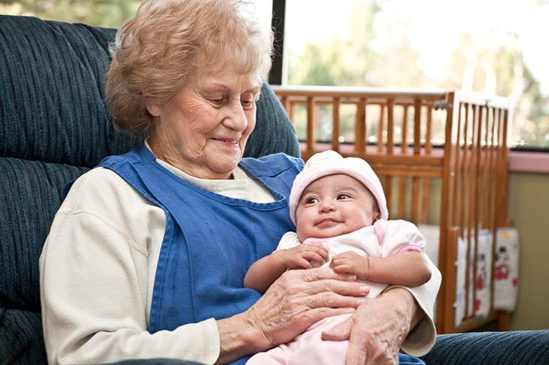 A senior woman holds a baby and smiles.