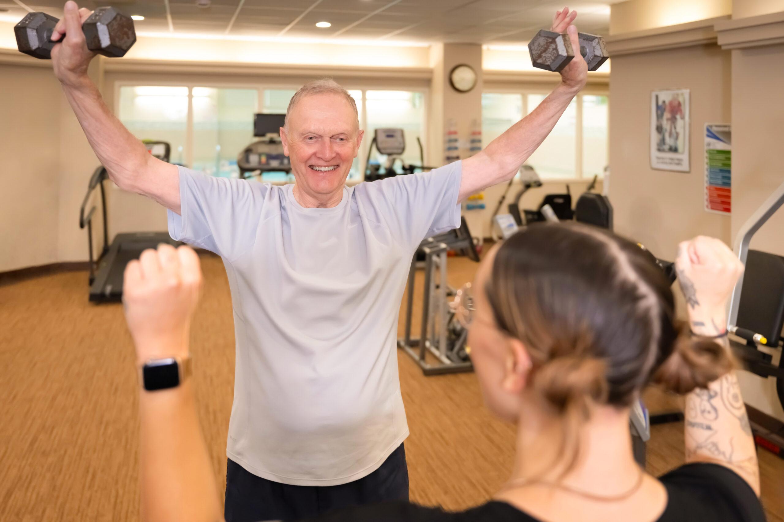 A smiling man does strength training with a personal trainer.