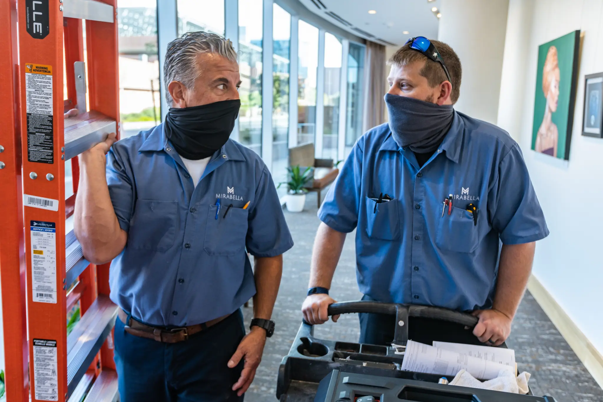 Two maintenance employees talk while holding equipment.